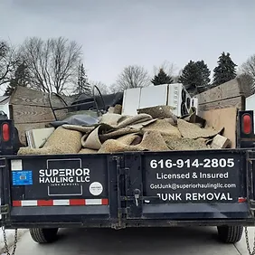 A red and white dump truck from Superior Hauling LLC carrying dirt and rocks on a sunny day.